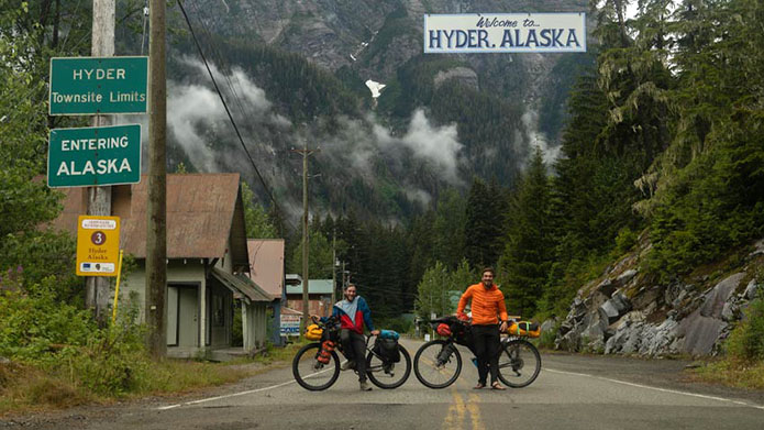 Ecotourism and outdoor leadership student Teegan Neame (right) and friend John Moreland (left), stand with their bikes under a "Welcome to Hyder Alaska" sign