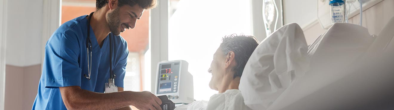 a young nurse placing a blood pressure cuff on a patient in a hospital bed.