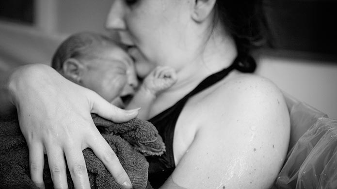 Close up photo of a new mother in a bathtub holding a newborn to her chest.