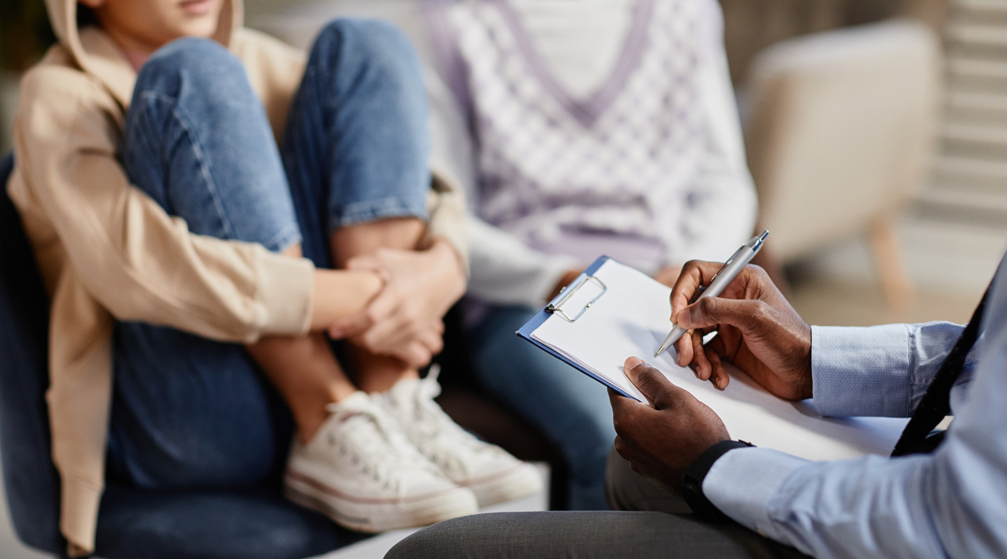 A pshychologyst takes notes on a clipboard in therapy session for a child.