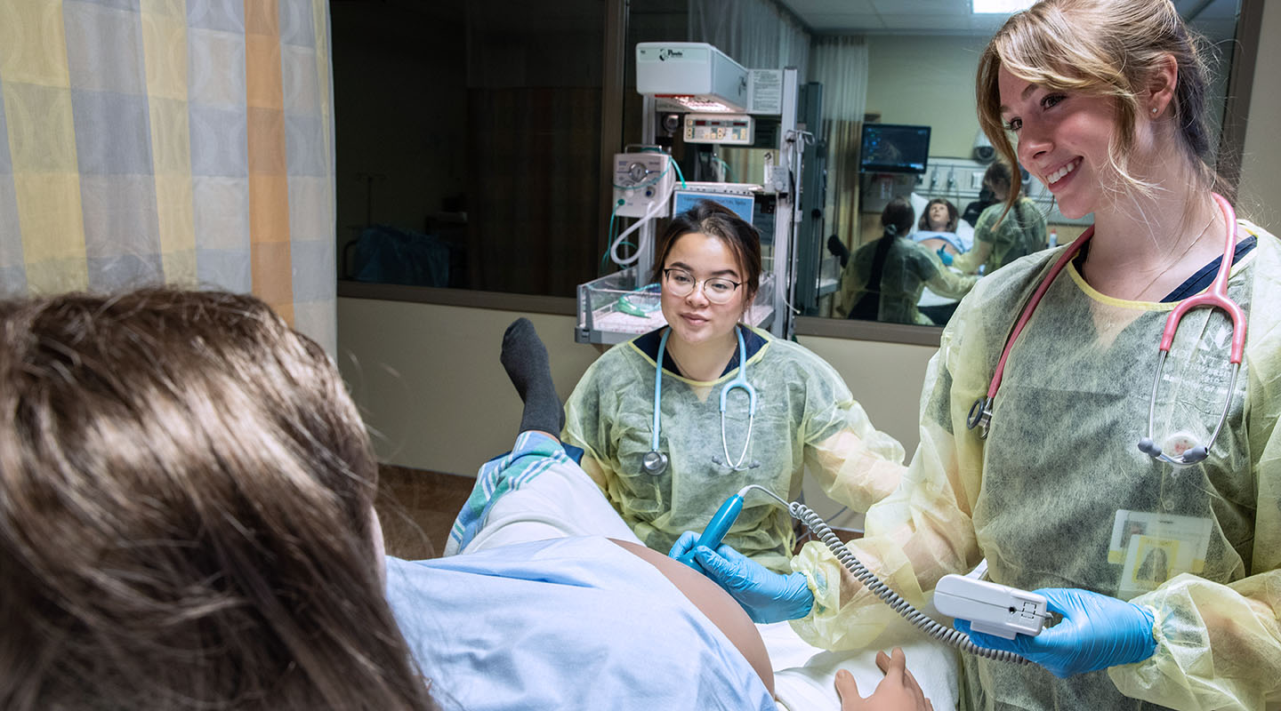 Two Mount Royal University midwifery students administering an ultrasound on a pregnant medical mannequin in the Health Simulation Learning Centre.
