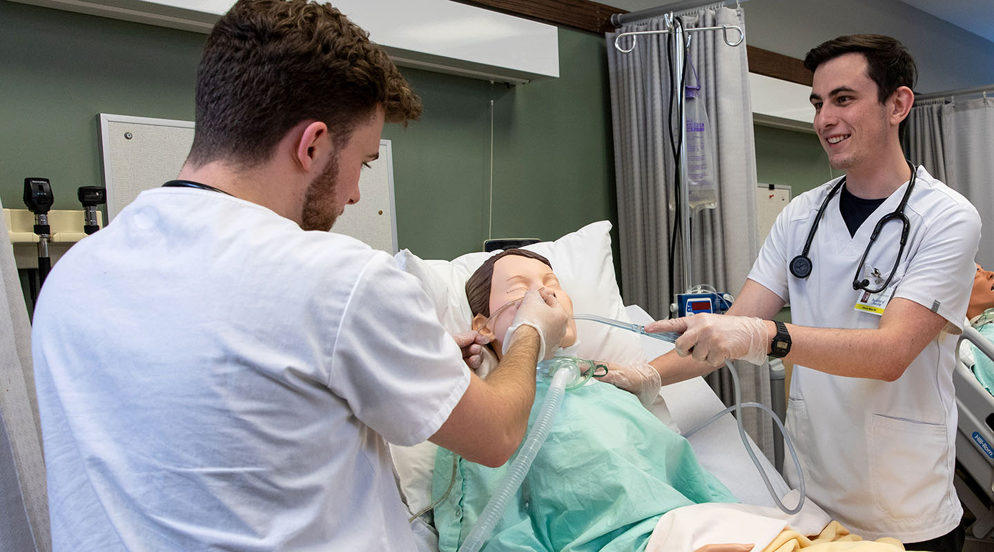 Two MRU nursing students practice medical procedures on a training mannequin in the Health Simulation Learning Centre.