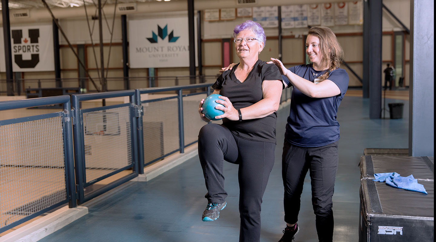 A senior patient holds a medicine ball while receiving guidance from a professional at the Mount Royal University recreation centre