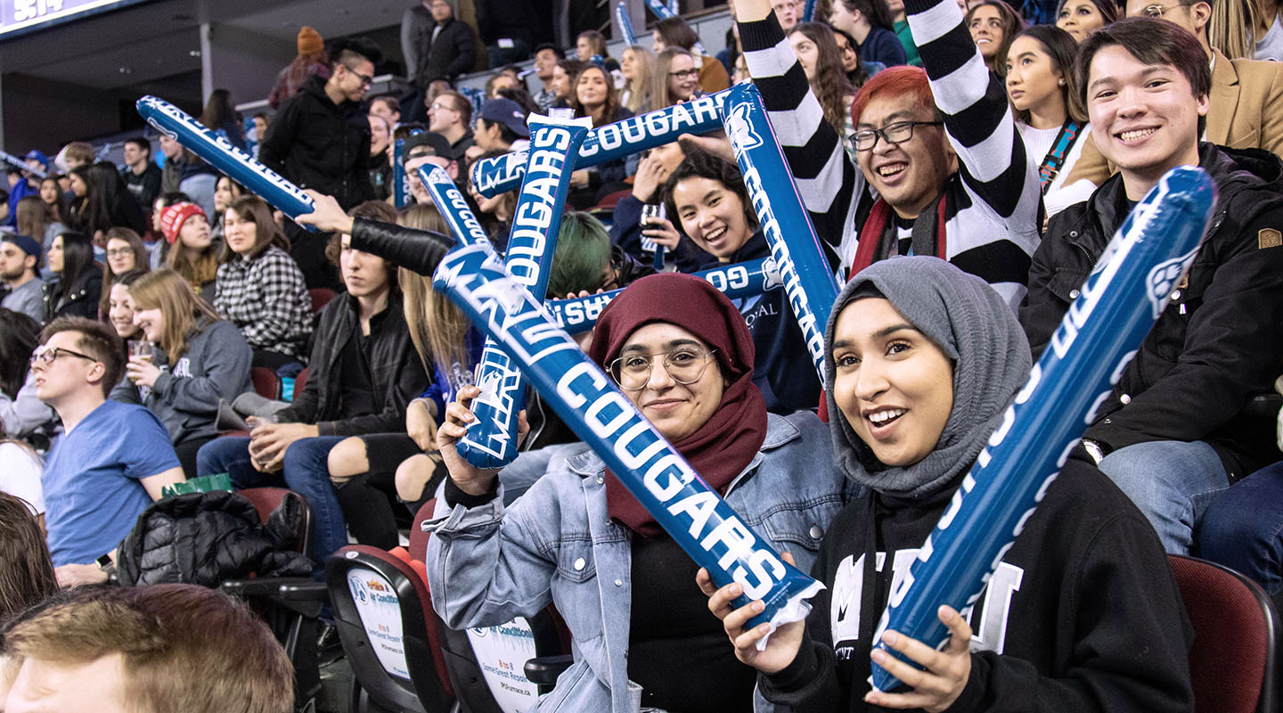 Mount Royal University Cougars fans smile and clap thunder sticks in the Scotiabank Saddledome.