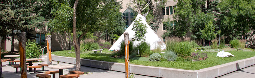 Mount Royal's Centennial Sundial Garden, with ourdoor tables and bences, a teepee and tree trunks carved with feathers.