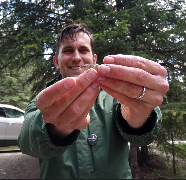 Jon happily holds a brook stickleback fish in front of him. 