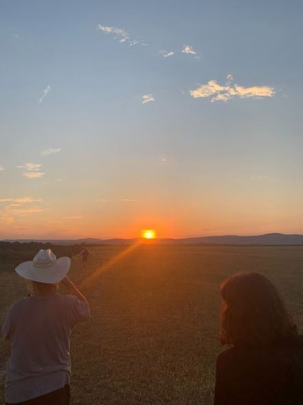 Sun setting in the background, with Alex Farmer tipping her cowboy hat towards the setting sun.
