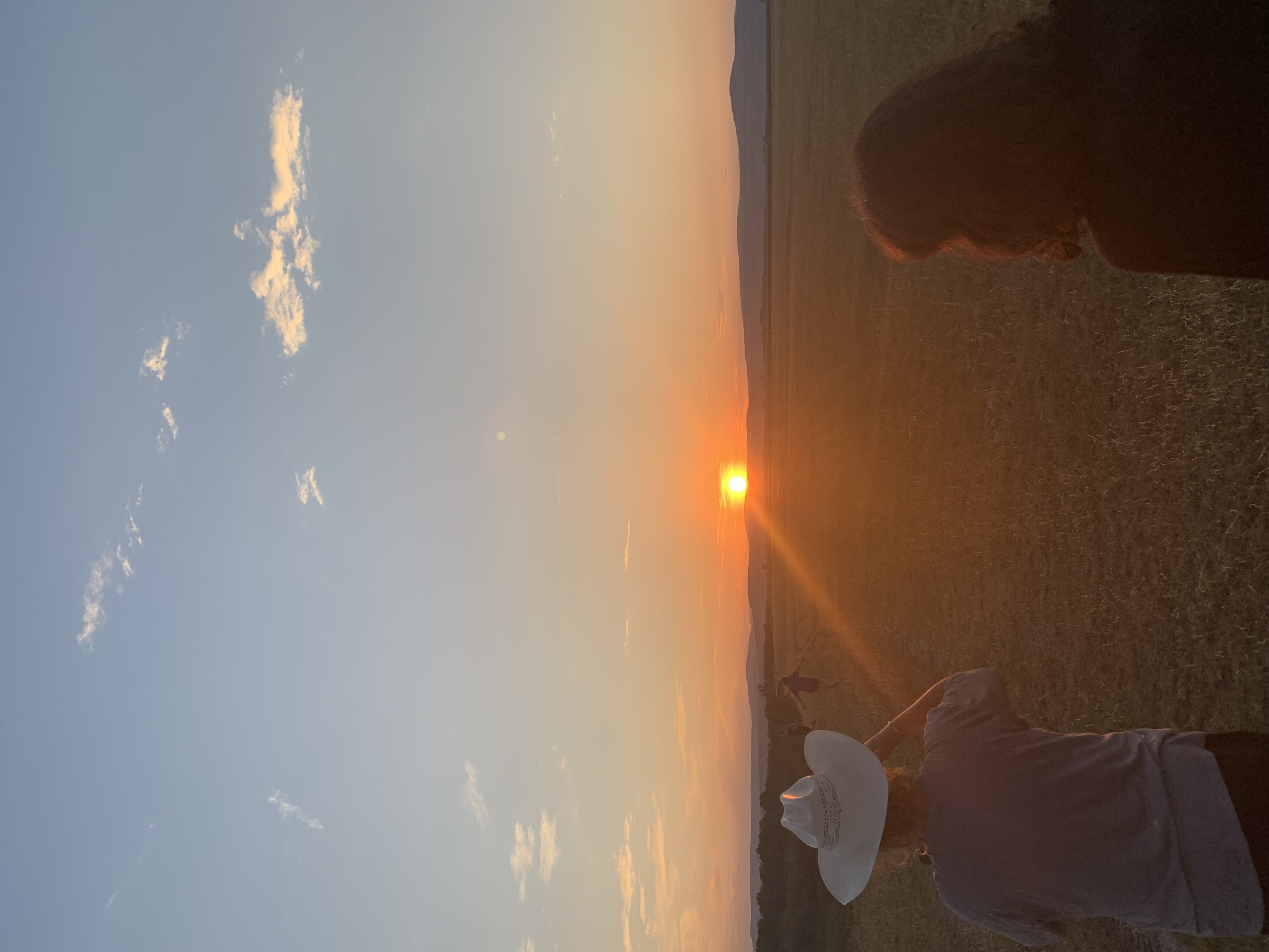 Two people with their backs facing the camera stare into the setting sun across a prairie field.