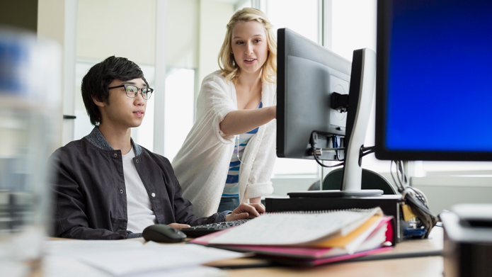 A professor working one-on-one with a student in a computer lab at Mount Royal University.