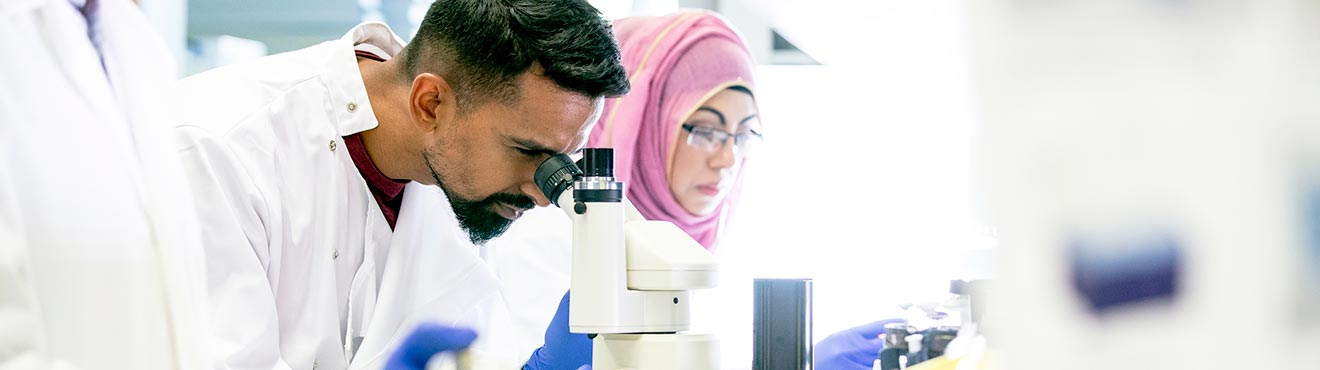 Two students working in a pab. One looks into a microscope..