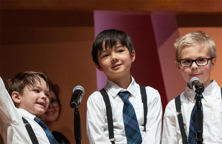 Three young boys standing behind microphones on stage