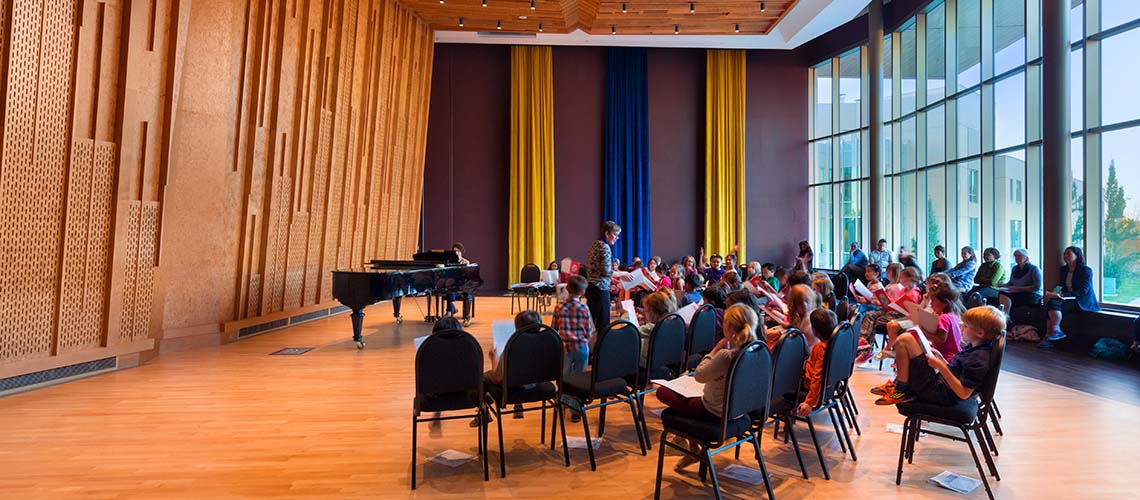 A group of children listening to an instructor in the TransAlta Pavillion in the Taylor Centre for the Performing Arts.