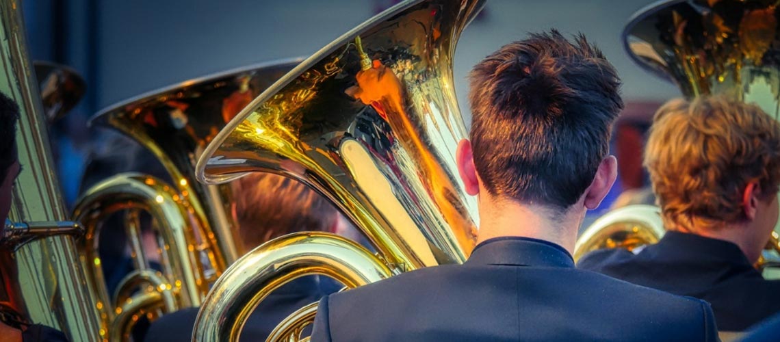 Photo of a group of musicians from behind in the brass section of an orchestra.