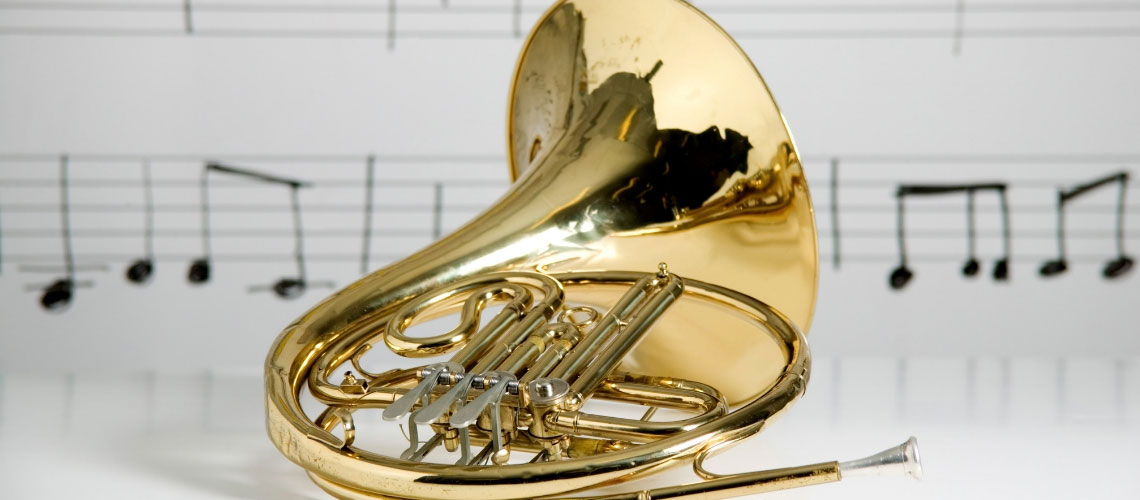Photo of a french horn in front of a wall covered in musical notation.
