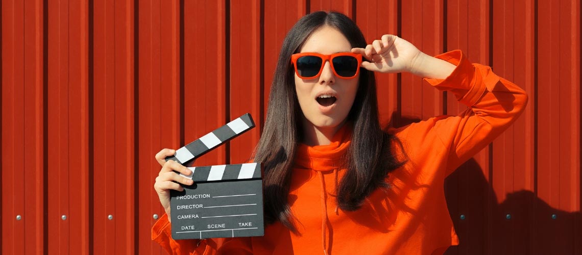 A young lady in sunglasses holding a clapperboard.