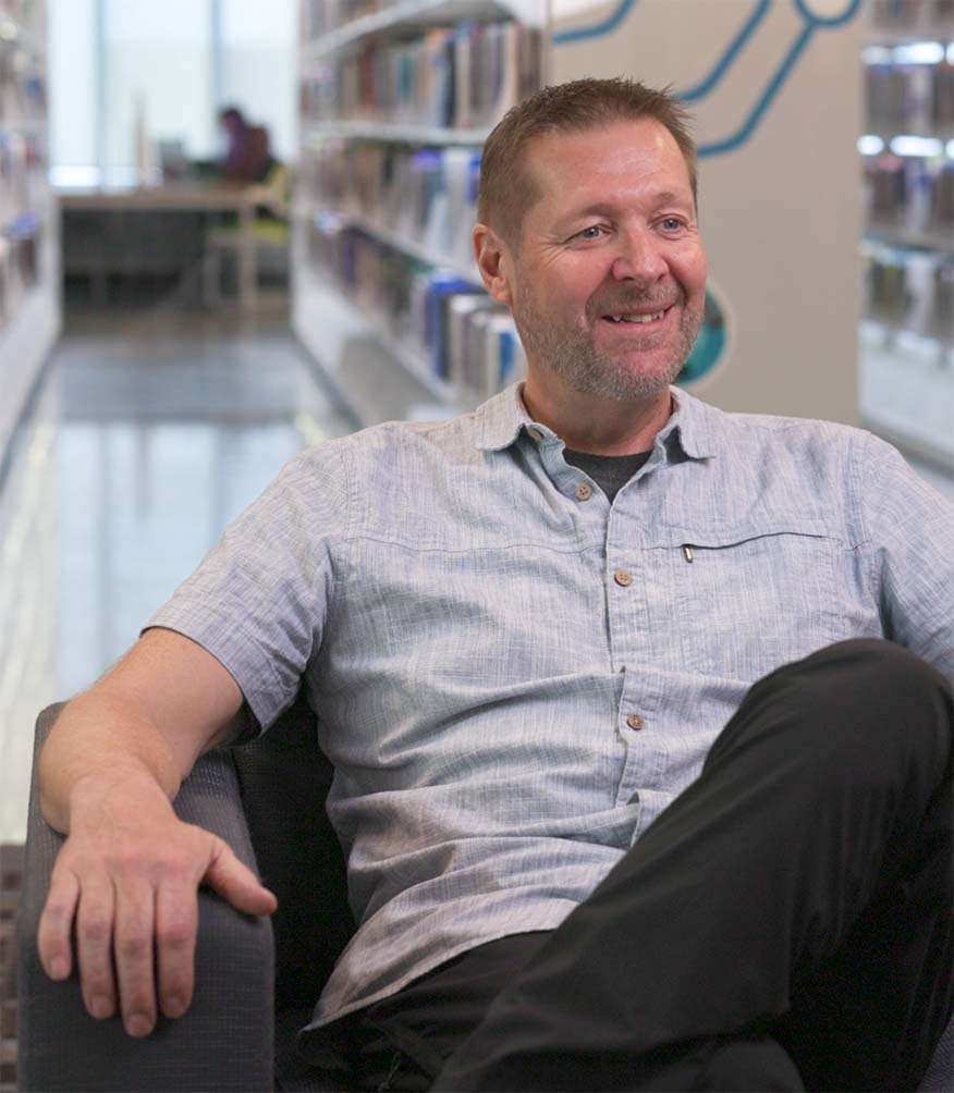 Dr. Anthony Chaston, PhD sitting in a chair in the Riddell Library and LEarning Centre.