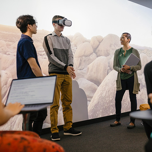 A person wearing VR goggles in the Immersion Studio. There are people around observing and taking notes.