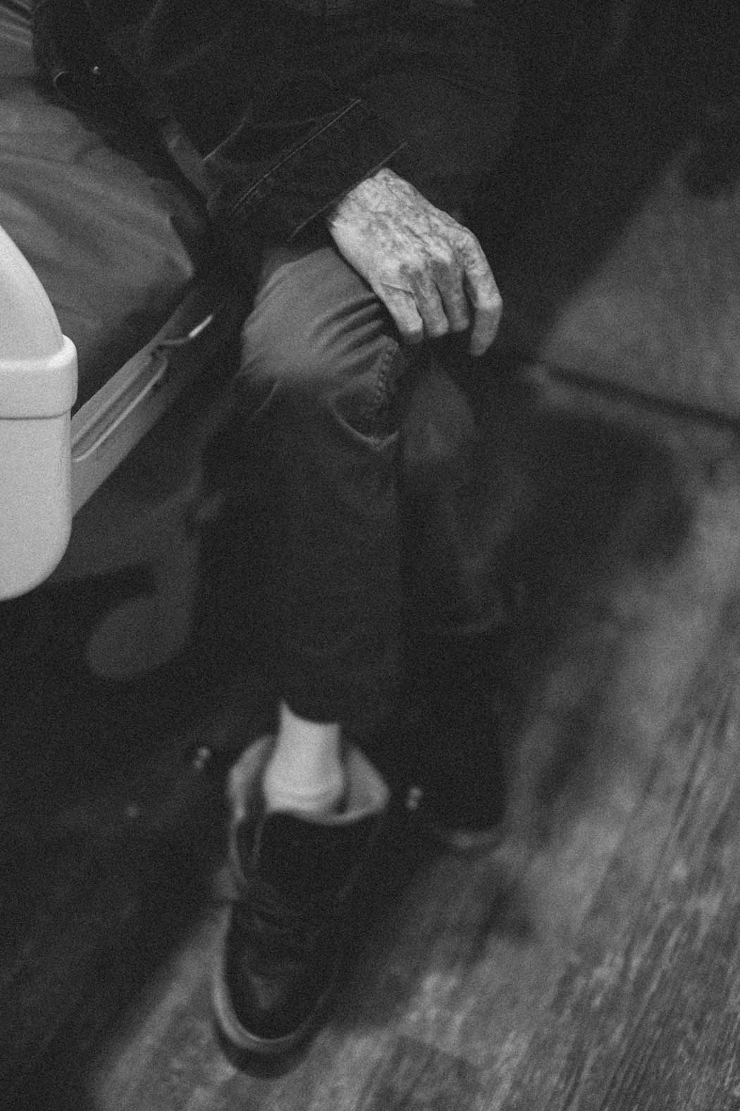 Black and white photo of a person, sitting with their legs crossed on a bed. The subject is only shown from the waist down