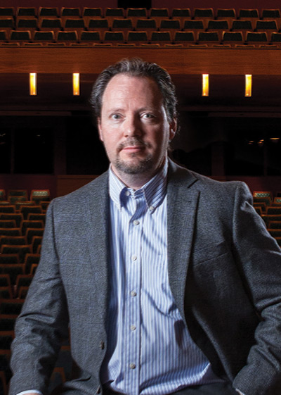 Brad Mahon perches on a stool in the center of the stage at the Bella Concert Hall