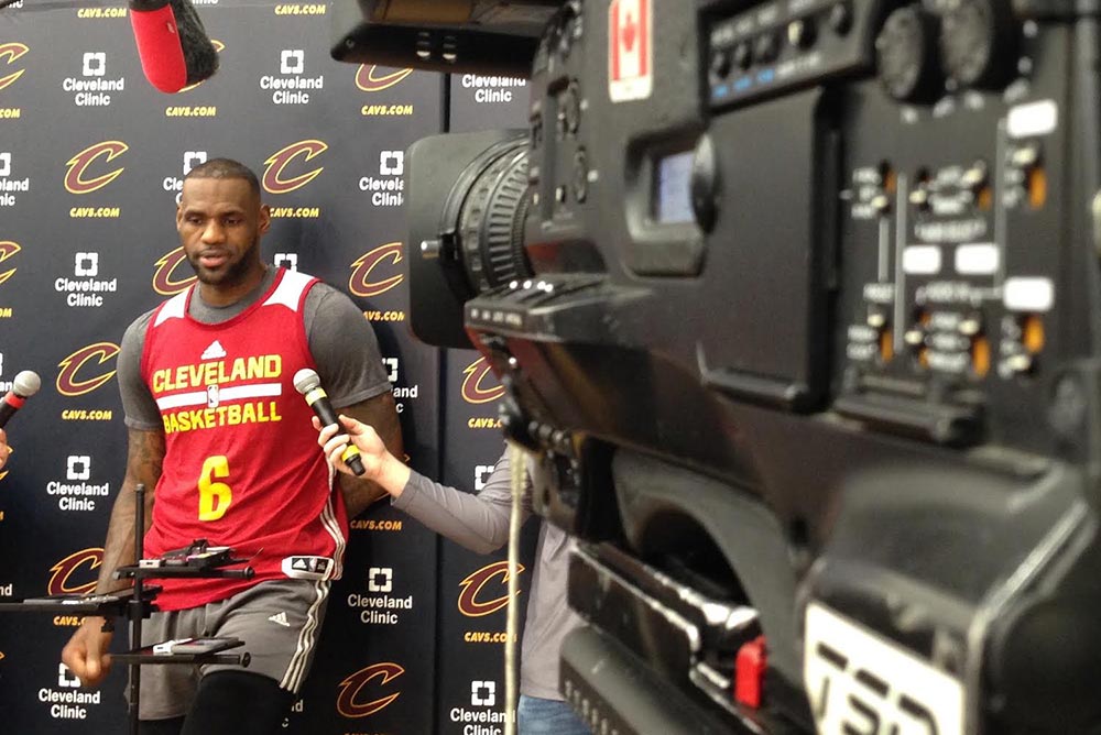 A Cleveland Cavaliers player framed by a large broadcasting camera.