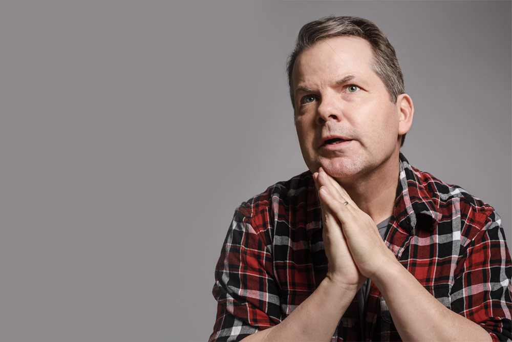 Photo of Bruce McCulloch with his hands pressed together as if in prayer. His chin rests gently against his hands.