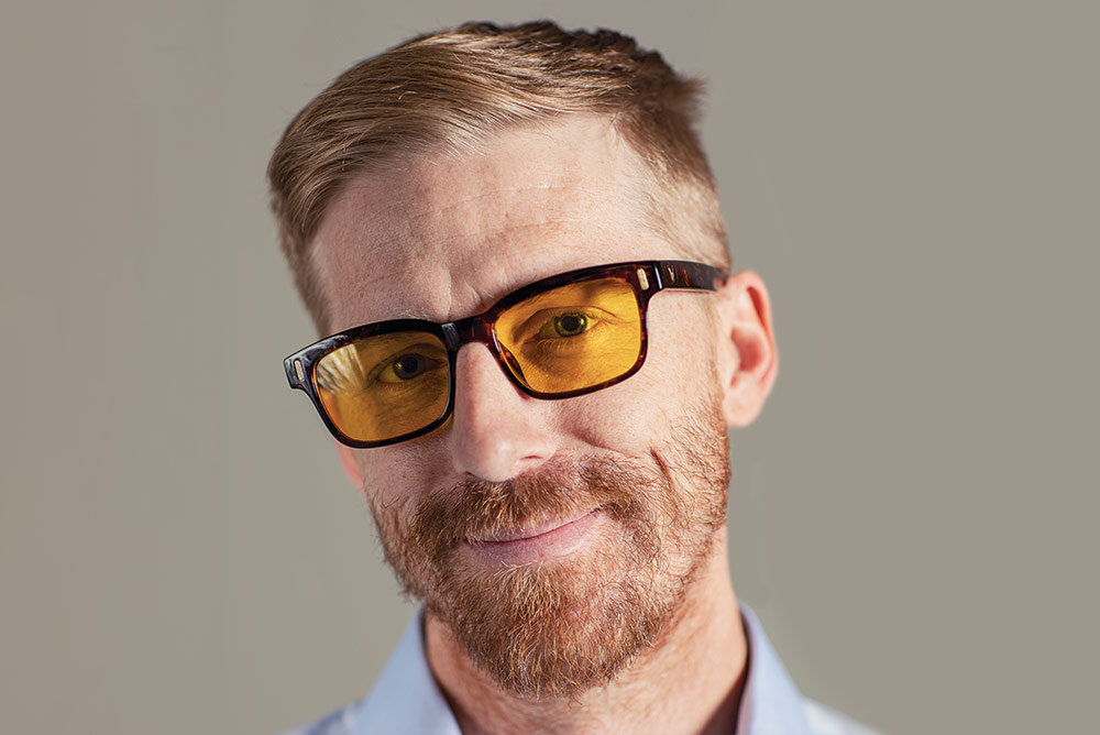 Straight on photo of alumnus Basil Kelly wearing yellow tinted glasses.