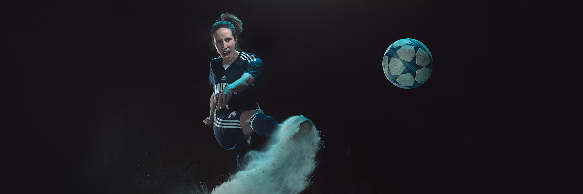 A member of the Women's Cougar's Hockey team in goalie gear takes a defensive stance in dramatic lighting and blue powder.