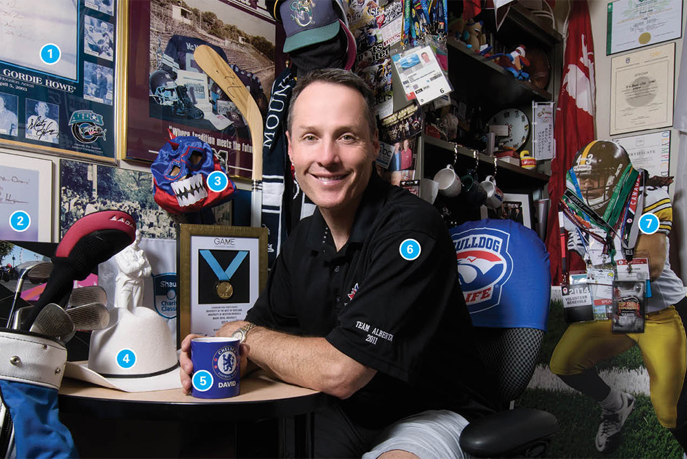 David Legg leans on his desk while surrounded by a plethora of sports memorabilia.