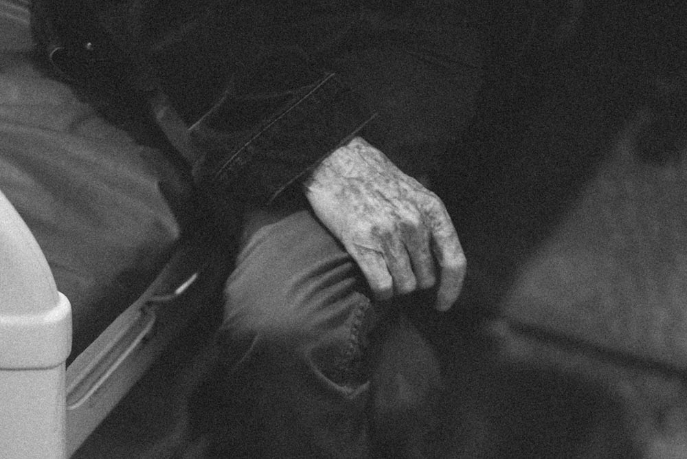 Black and white photo of a person, sitting on a bed with their legs crossed on a bed.