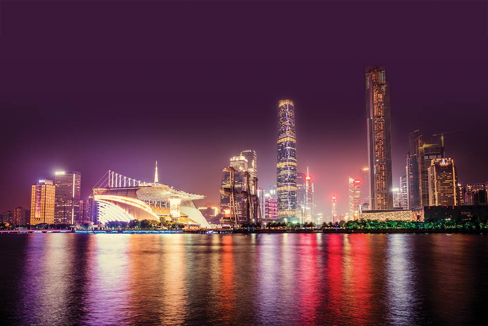 Nighttime photo of the skyline of Guangzhou, China. The city's bright lights reflect on the waters of the bay.