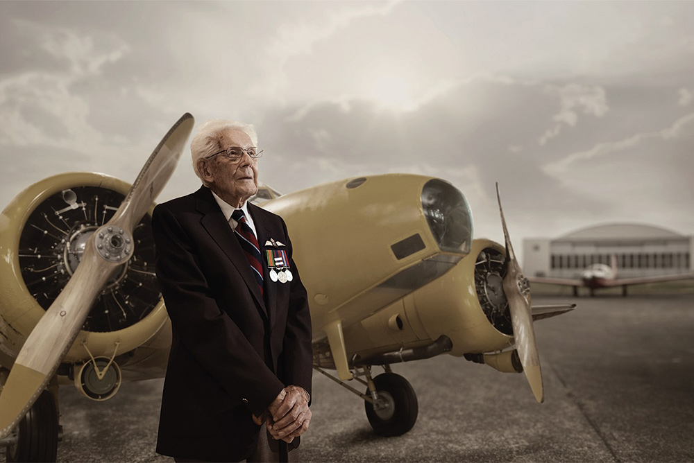 Andy Robson stands stoically in front of an airplane.