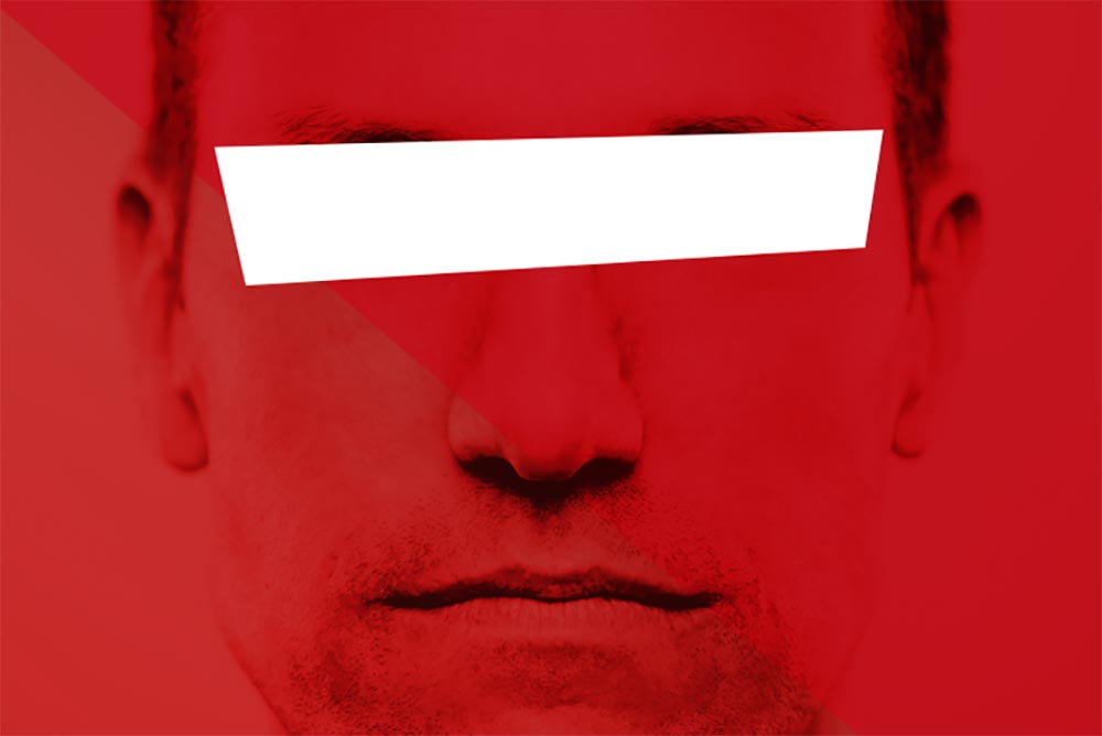 A portrait of a man staring into the camera. A white censor bar covers his eyes.