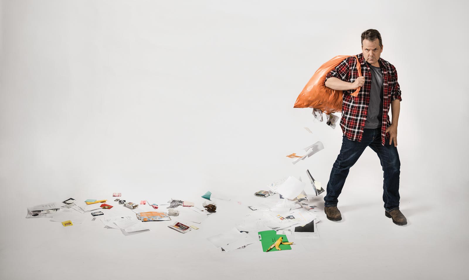 Photo of Bruce McCulloch walking holding a garbage bag. A variety of school products are strewn behind him.