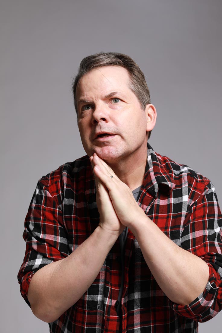 Photo of Bruce McCulloch with his hands pressed together as if in prayer. His chin rests gently against his hands.