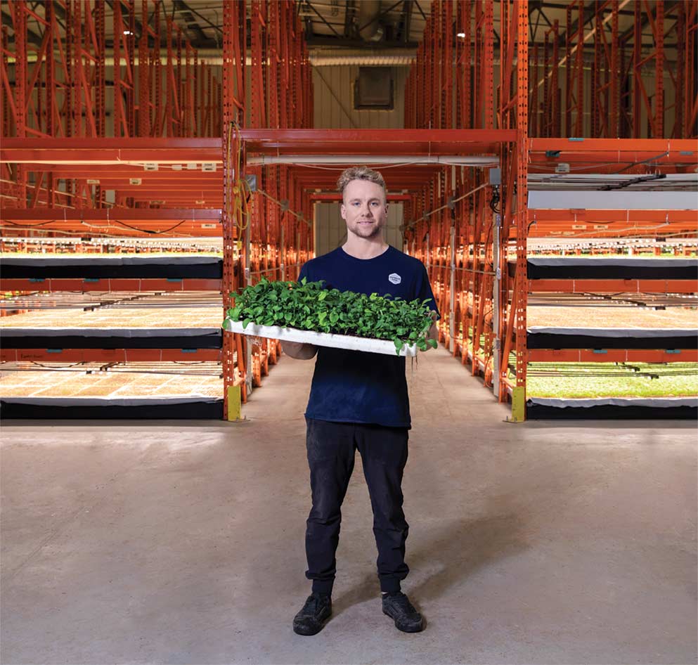 Paul Shumlich holding a tray of plants in front of a warehouse of hydroponic plants