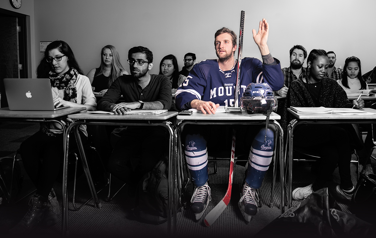 Photo of Ryan Gyaki sitting in a classroom in full hockey equipment
