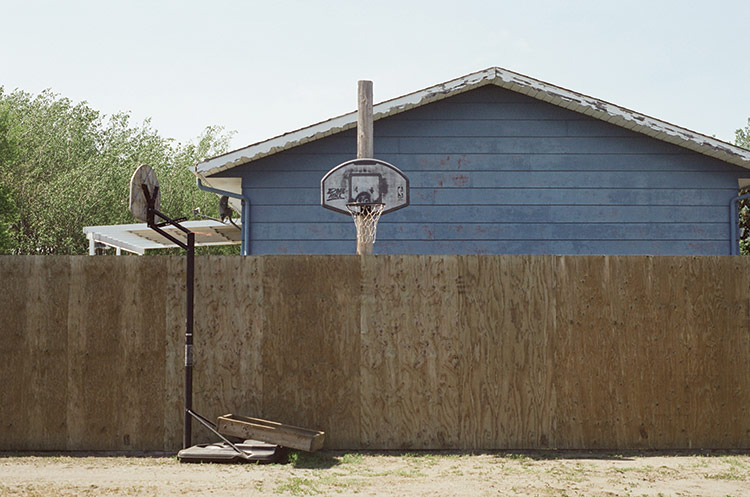 A photo of a older house behind a rustic wooden fence. Two basketball nets can be seen.