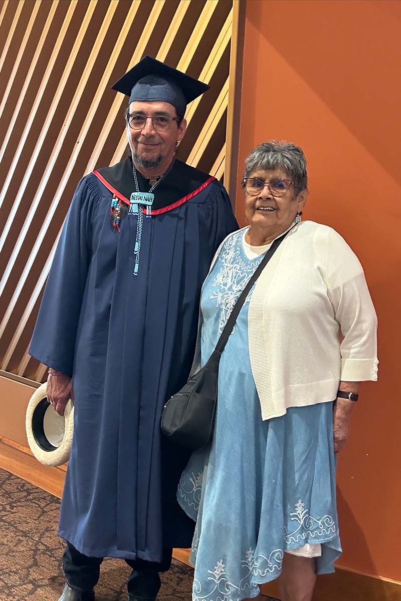 Douglas Barkley in his graduation regalia stannding beside his mother