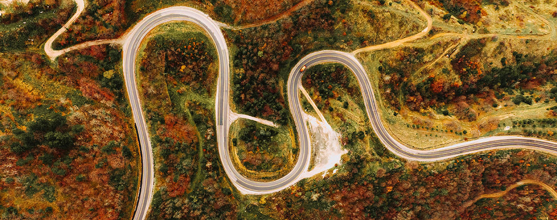 Top down photo of a winding road weaving through a forest of fall colours.