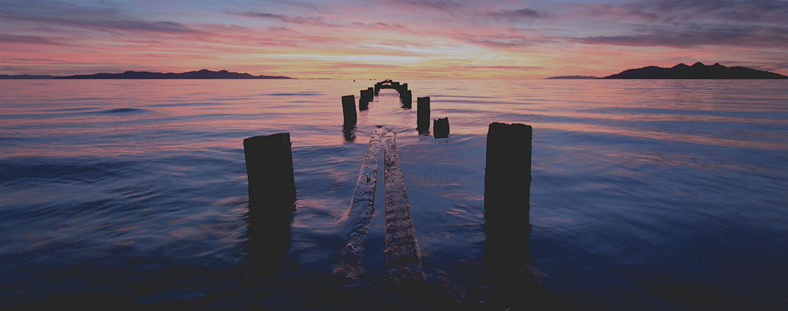 Photo of a large body of water at sunset and a series of dock piling sticking out of the water.