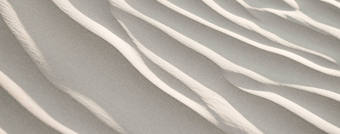 Close up photo of ripples in light-coloured sand.