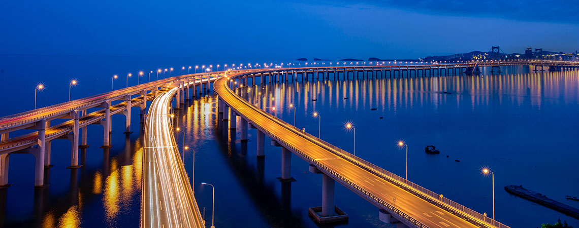 Bridge at night curving over towards a city.