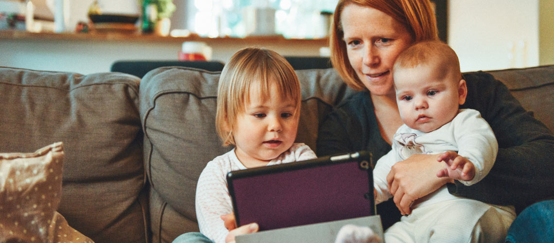 A mom and two children sitting on a couch with an iPad.