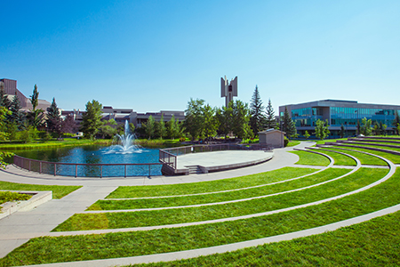 An outdoor stage in front of a pond with a fountain with rings of grassy steps forming a seating area.