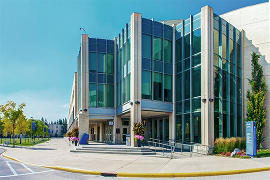 The glass covered corner of an otherwise concrete building by a campus greenspace.