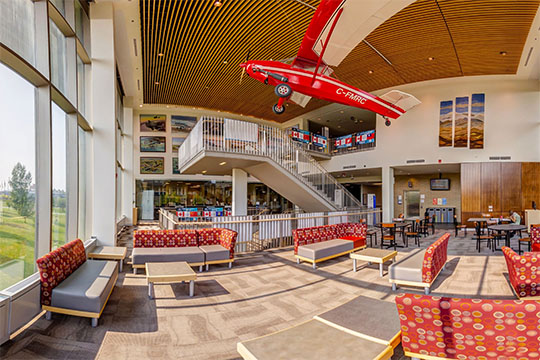 Couches and low tables beside a open stairway underneath a plane hanging fro the ceiling.