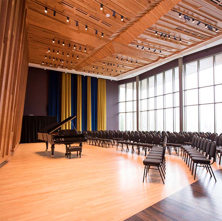 An recital room with a grand piano and rows of chairs.