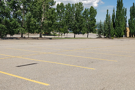 An empty parking lot in front of a row of trees and an intersection.