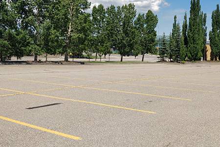 An empty parking lot in front of a row of trees and an intersection.