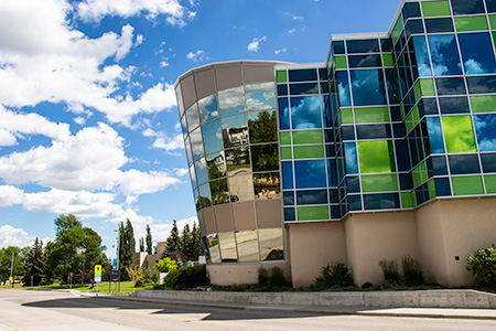 A brick building with a curved glass section made of bright green and blue panels.